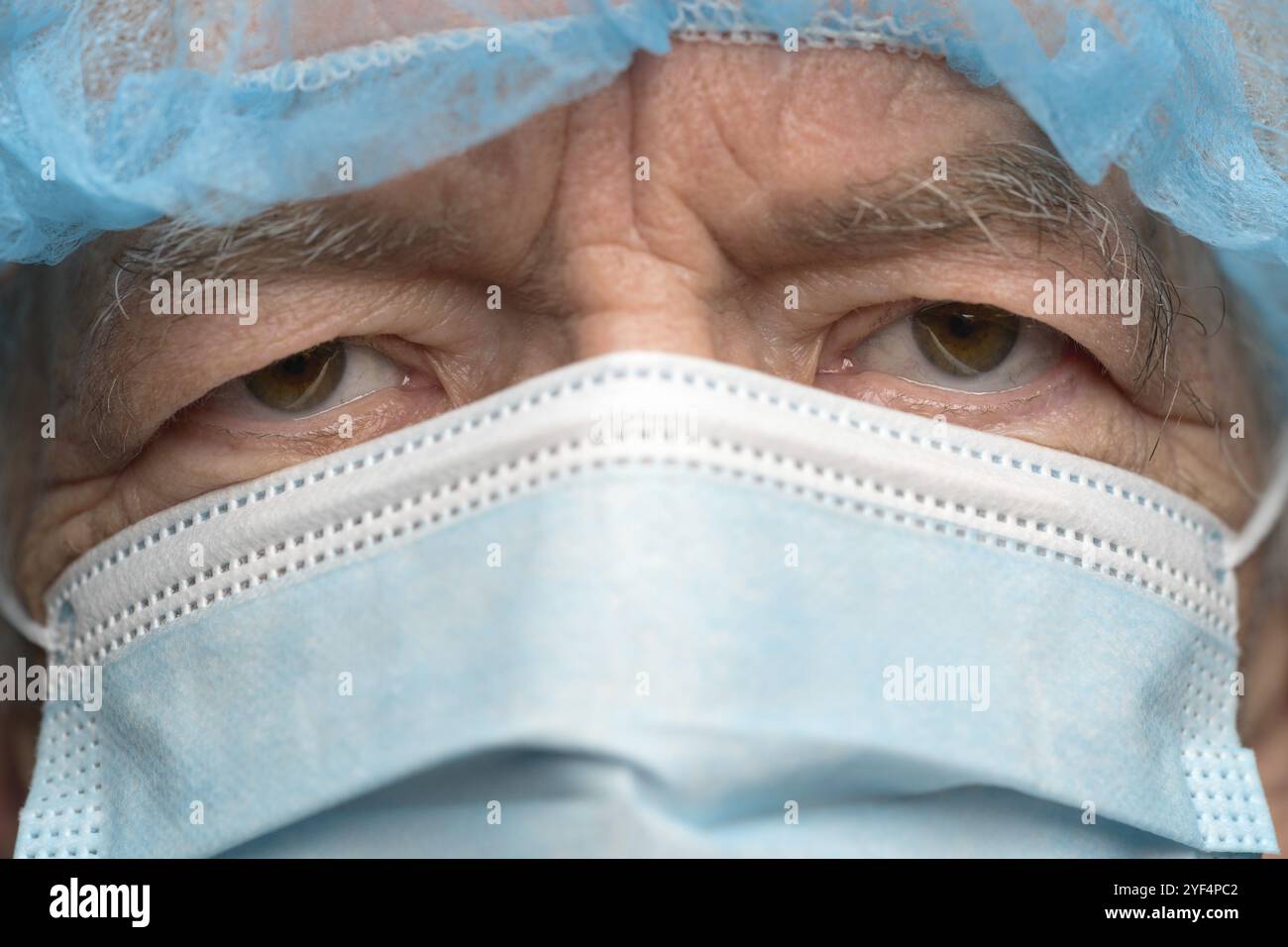 Close up portrait of sad senior adult dressed in surgical face mask with ear straps, covering nose from SARS, virulently infectious disease corona vir Stock Photo