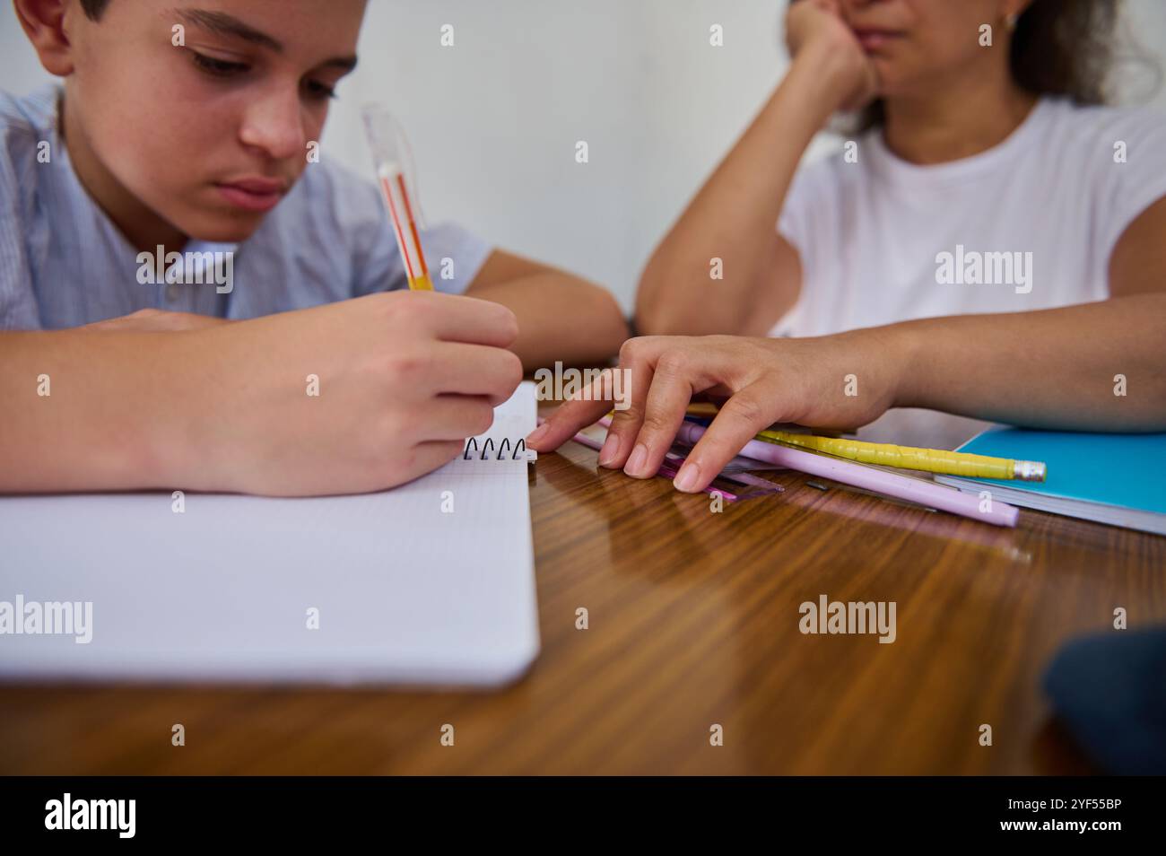 A young boy intensely writes in a notebook while his mentor looks on ...