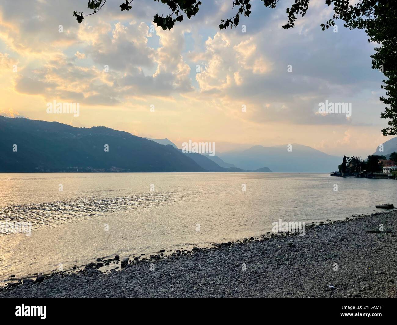 Soft sunset at blue hour on Lake Como, northern Italy. View from the beach to the lake and mountains behind, with clouds and fog in the sky. Peaceful - Smartphone Captured Stock Image