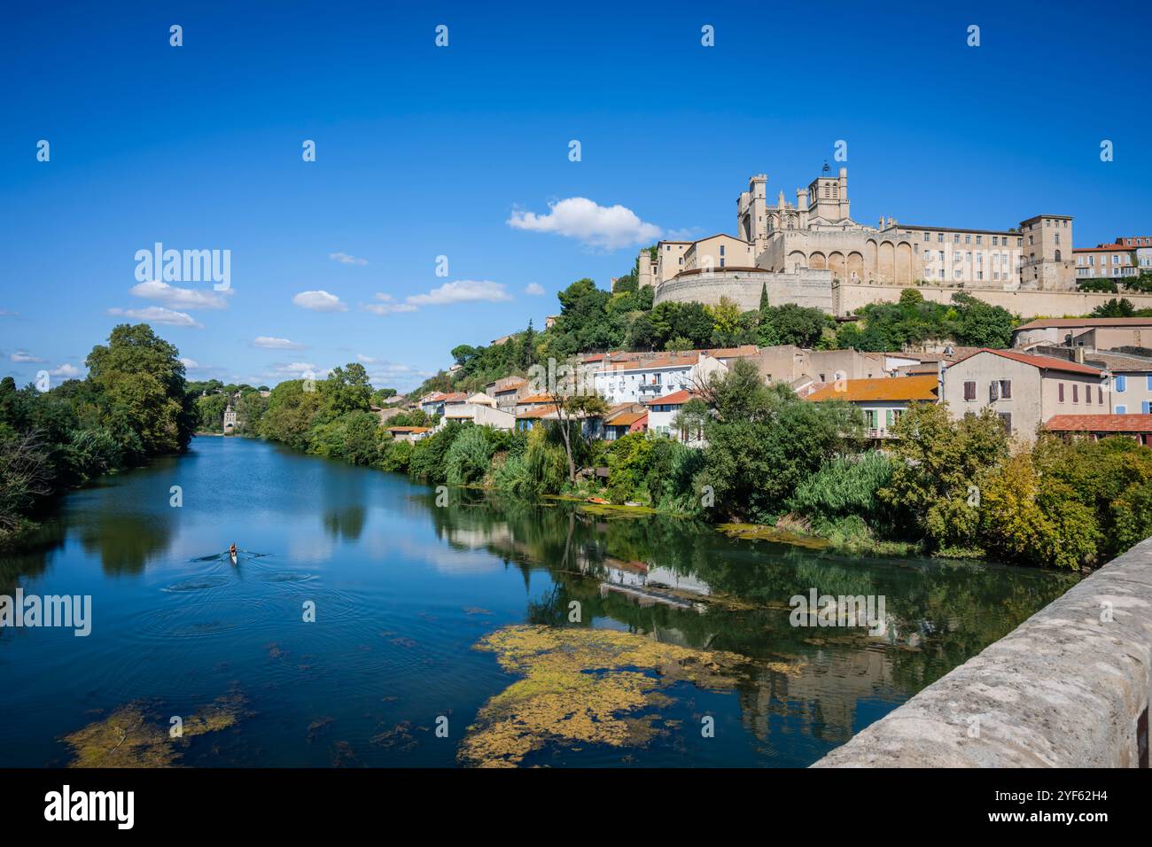 A female sculler on the River Orb with Beziers Cathedral on the hilltop, viewed from the famous bridge, Occitanie region, France. Stock Photo
