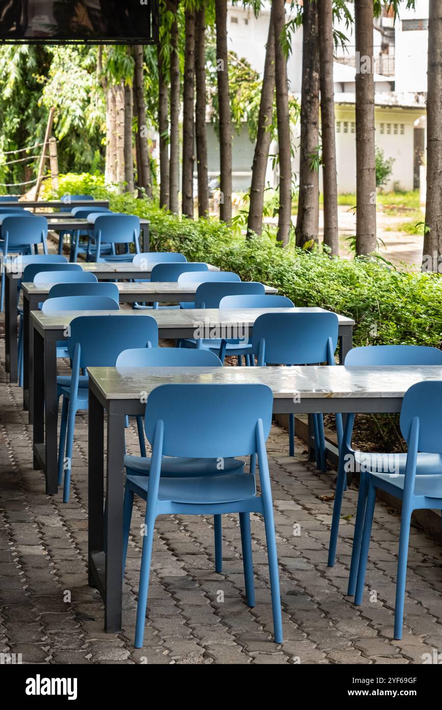 Outdoor cafe with wooden tables, stools on a city street. Wooden tables and blue chairs set up at an outdoor cafe on a sunny summer day. A cozy outdoo Stock Photo