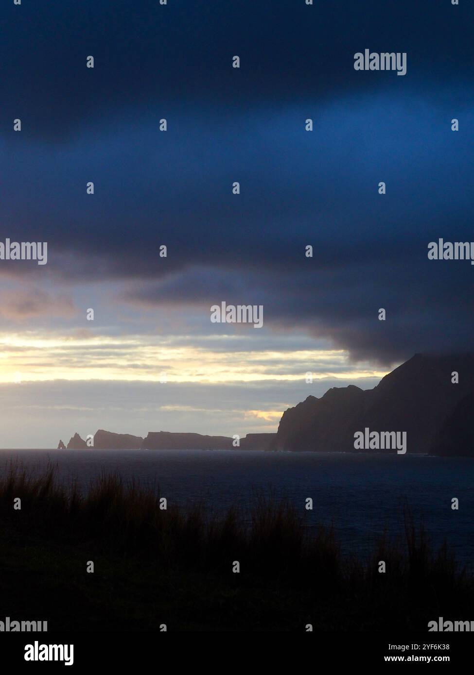 A stunning sunset over the ocean, with dark, dramatic clouds and rugged ...