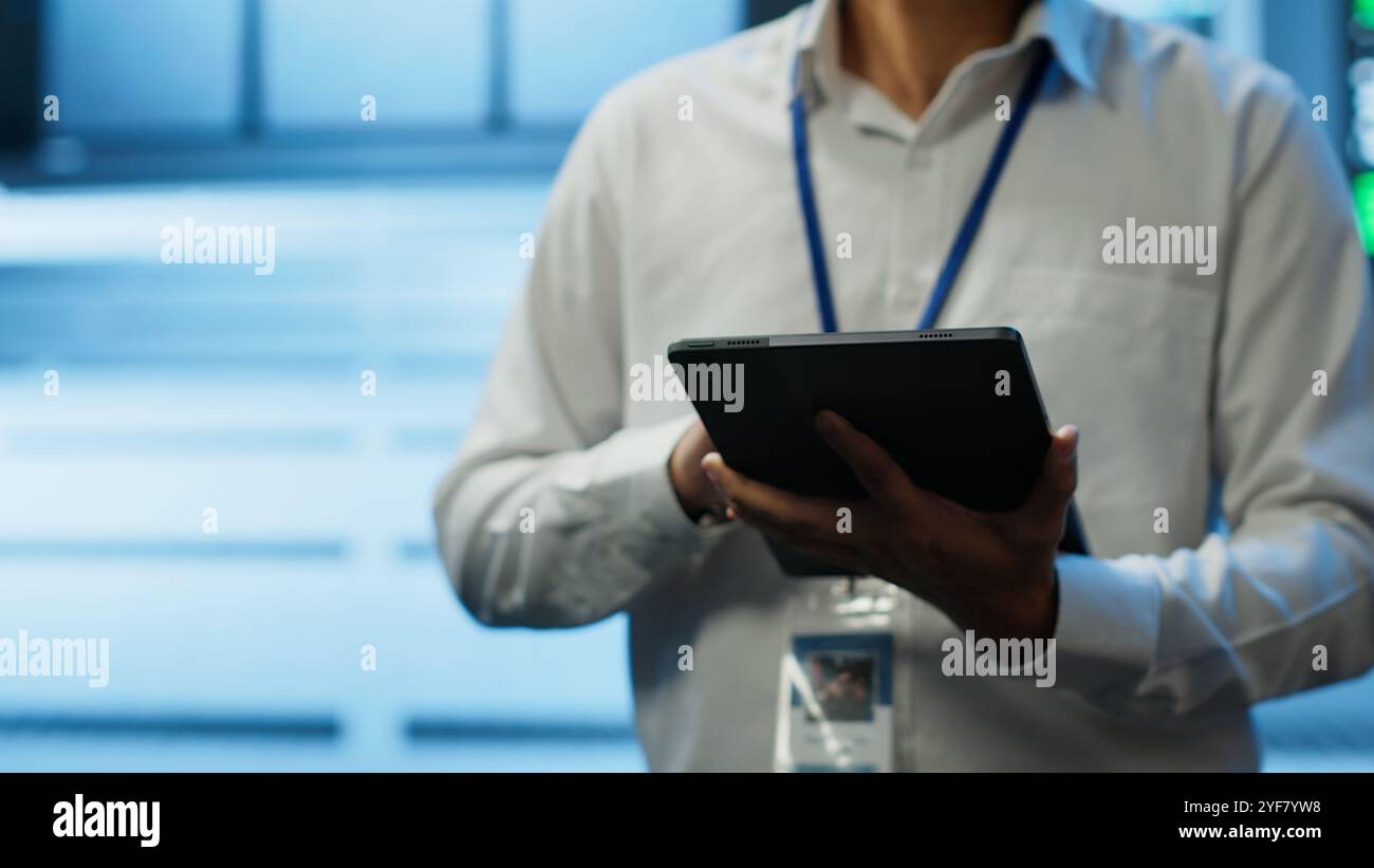 Software developer walking in data center, managing and maintaining databases, ensuring data integrity and security. Close up of man updating server room mainframe systems using tablet, camera A Stock Photo