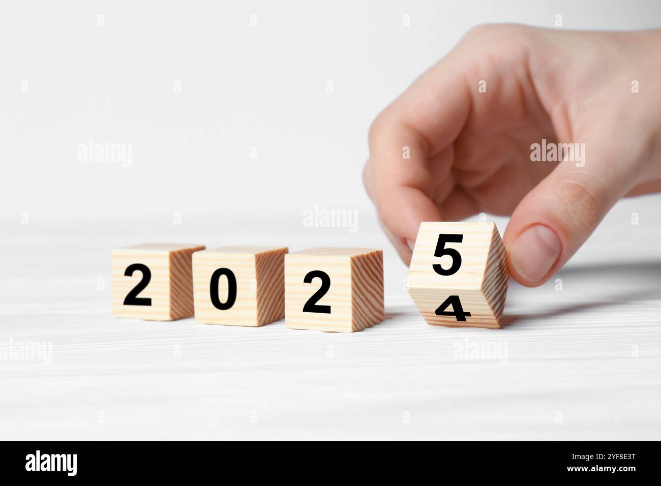 2025 New Year. Woman turning wooden cube on white table, closeup Stock Photo