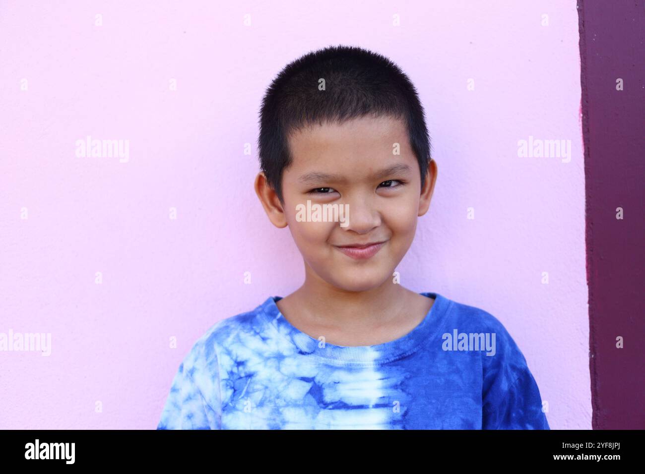A cheerful boy with short hair smiles confidently against a pink wall ...