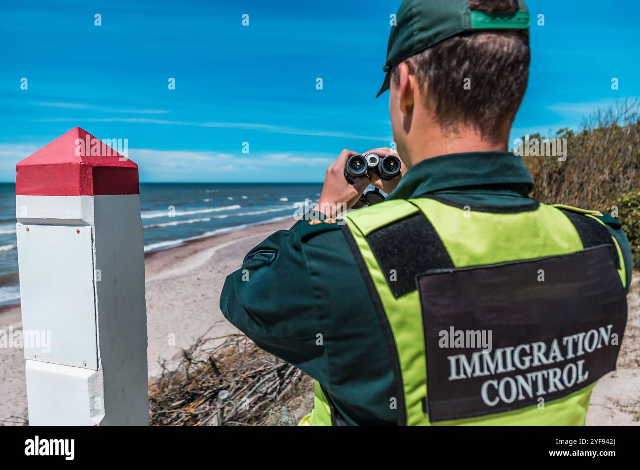 Immigration control officer surveying the coast with binoculars ...