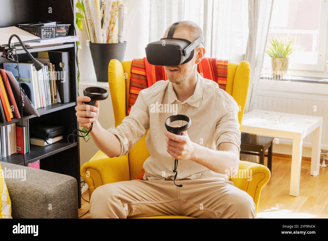 Mid adult man wearing virtual reality headset while playing video game at home Stock Photo