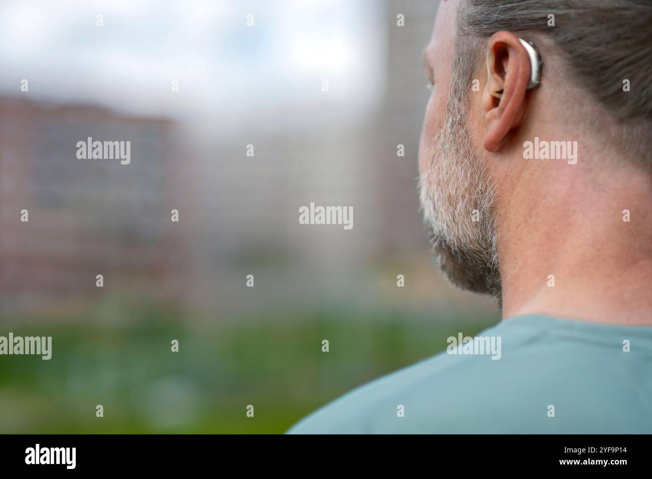 Rear view of man with gray beard wearing hearing aid device Stock Photo