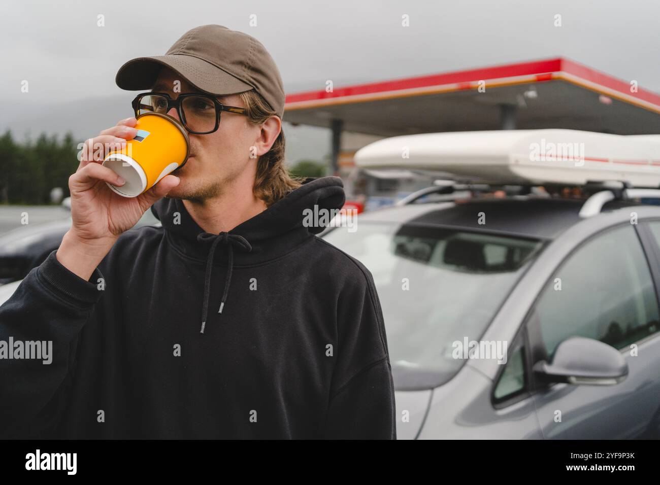 Handsome young man drinking coffee by car Stock Photo