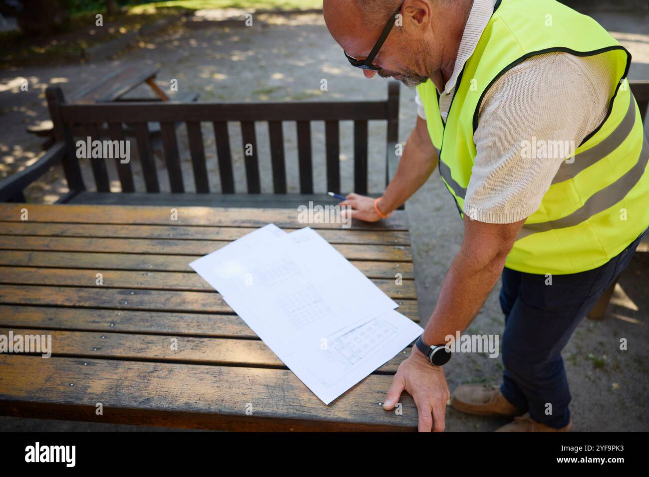 High angle view of male architect in reflective clothing examining blueprint kept on table Stock Photo