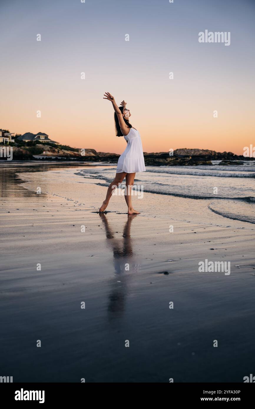 Woman in white dress stretches her arms up on the beach at sunset Stock ...