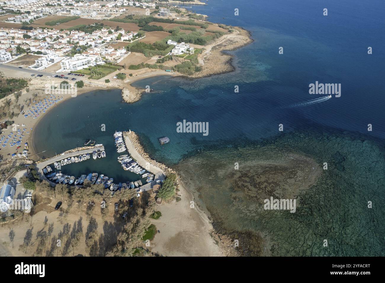 Aerial drone view of fishing harbour and sandy beach. Agia Triada people swimming and fishing boats moored at the harbor. Protaras Paralimni Cyprus Stock Photo