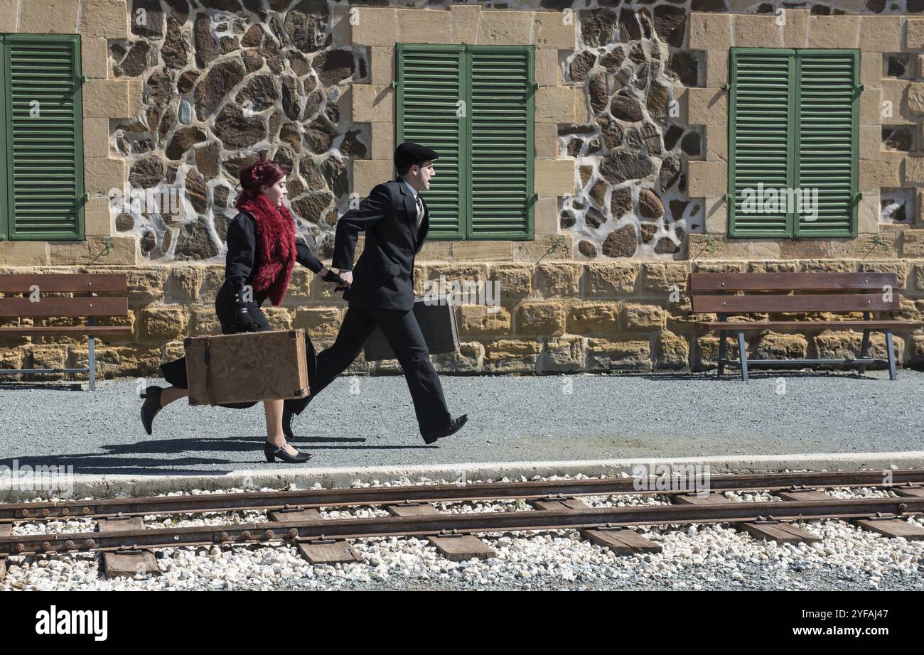 Young couple with vintage suitcase running fast outside a train station to catch the last train for journey Stock Photo