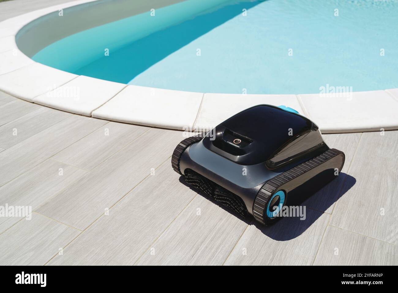 A robotic pool cleaner in front of a outdoor swimming pool with bright blue water, ready for efficient underwater cleaning and debris removal. Space for text Stock Photo