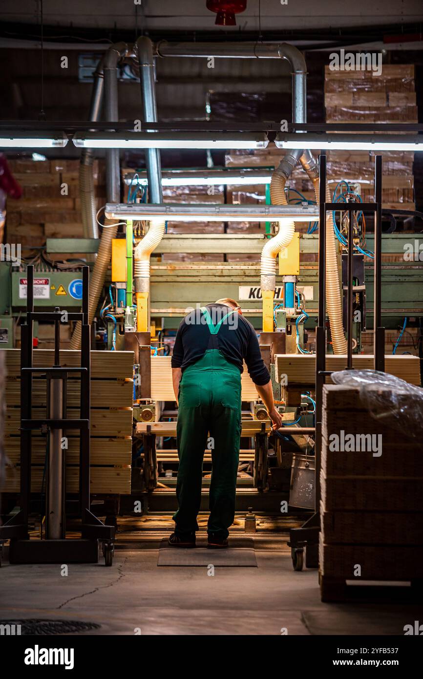 worker operates a computerized machine in a woodworking factory, processing large wooden beams in an industrial setting Stock Photo