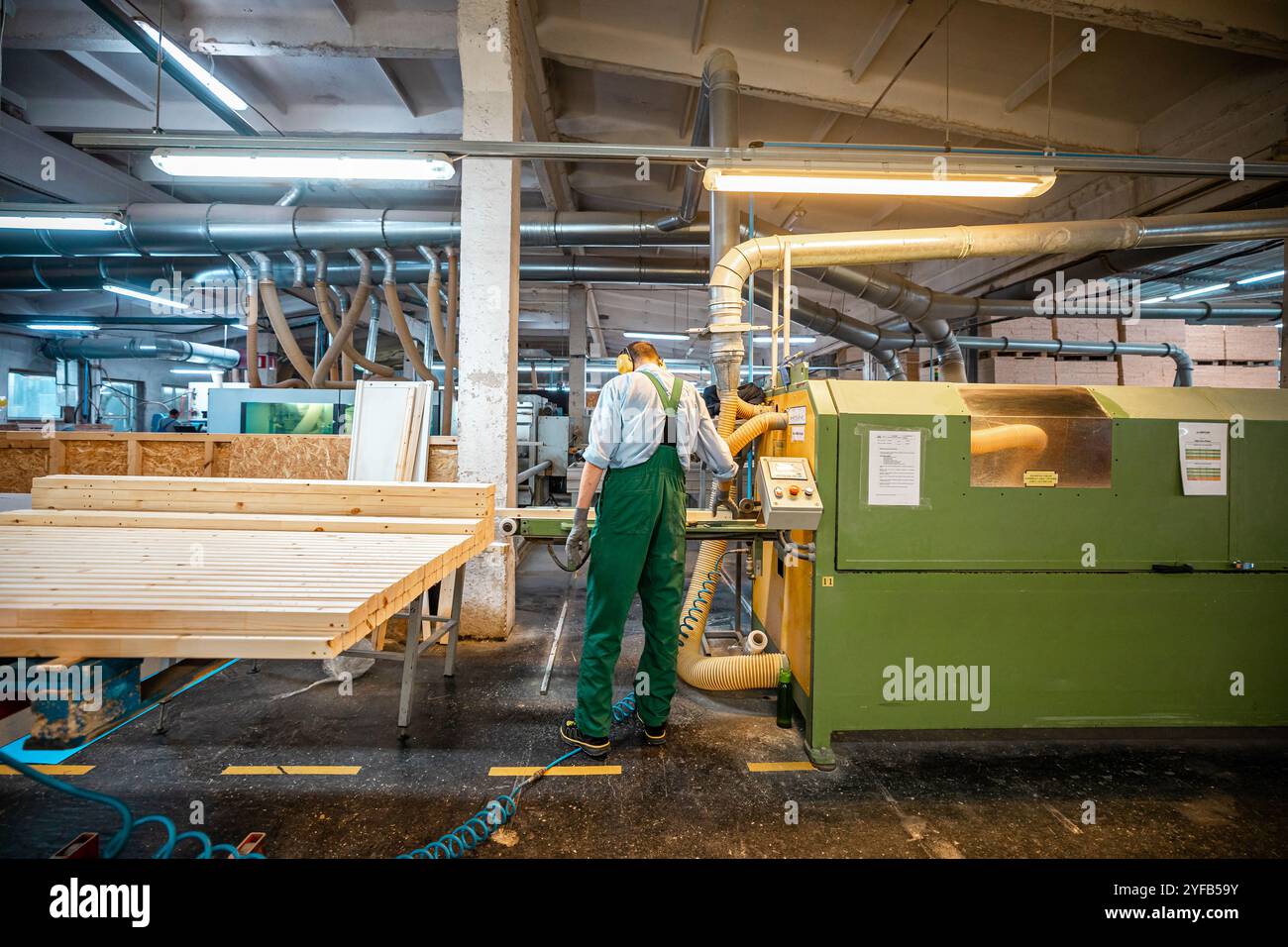 worker operates a computerized machine in a woodworking factory, processing large wooden beams in an industrial setting Stock Photo