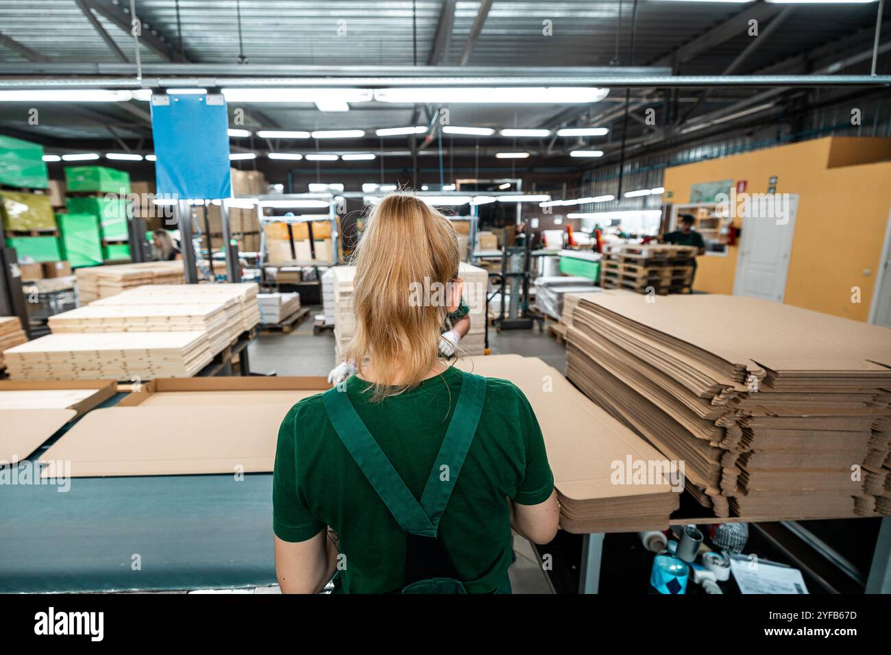 Worker handling stacks of wooden planks in a woodworking factory, preparing materials for further processing under industrial lighting Stock Photo