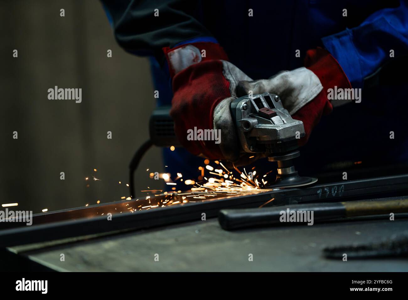 Craftsman using an angle grinder, creating bright sparks while working on a metal frame in the workshop. Stock Photo