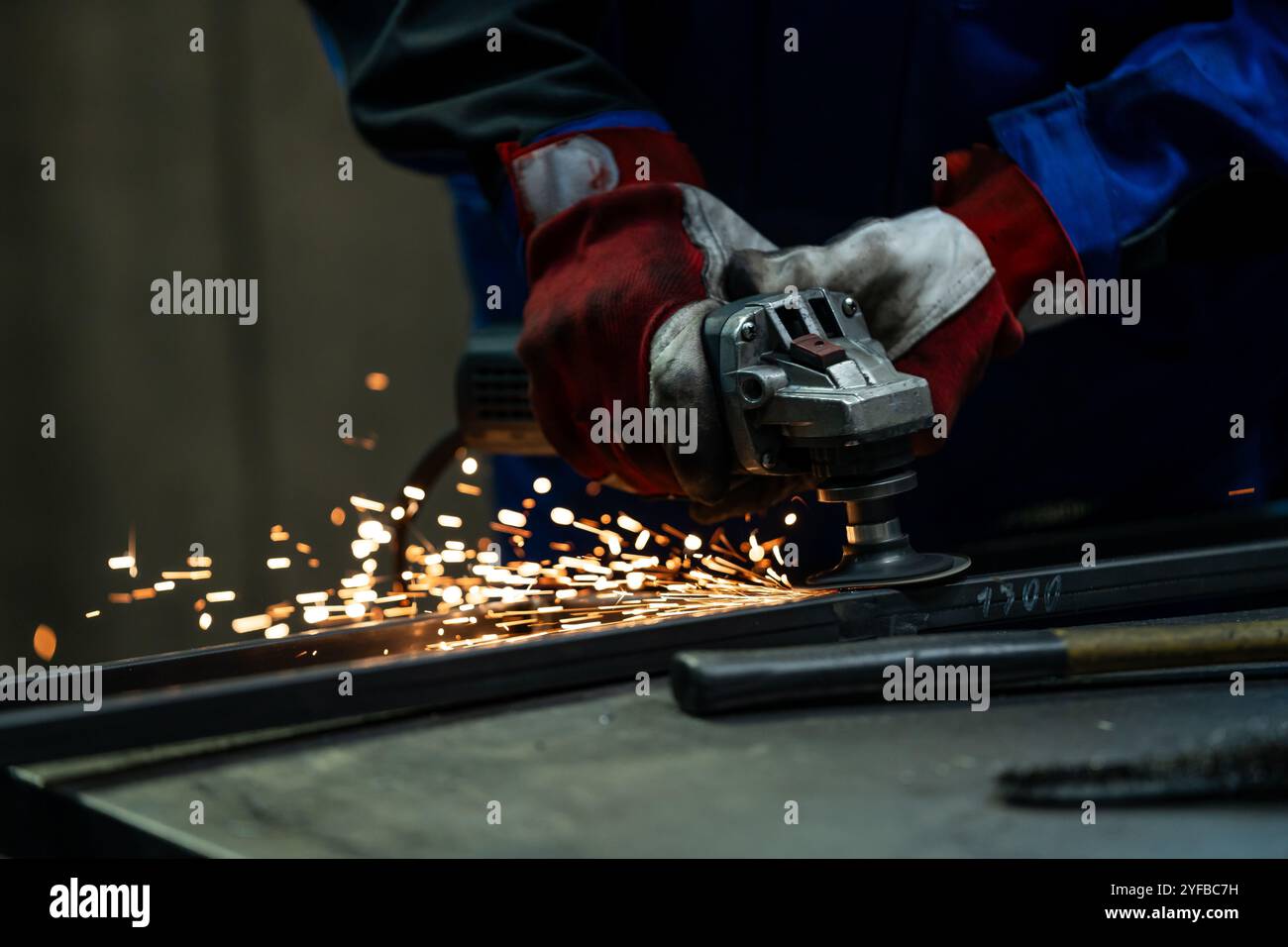 Craftsman using an angle grinder, creating bright sparks while working on a metal frame in the workshop. Stock Photo