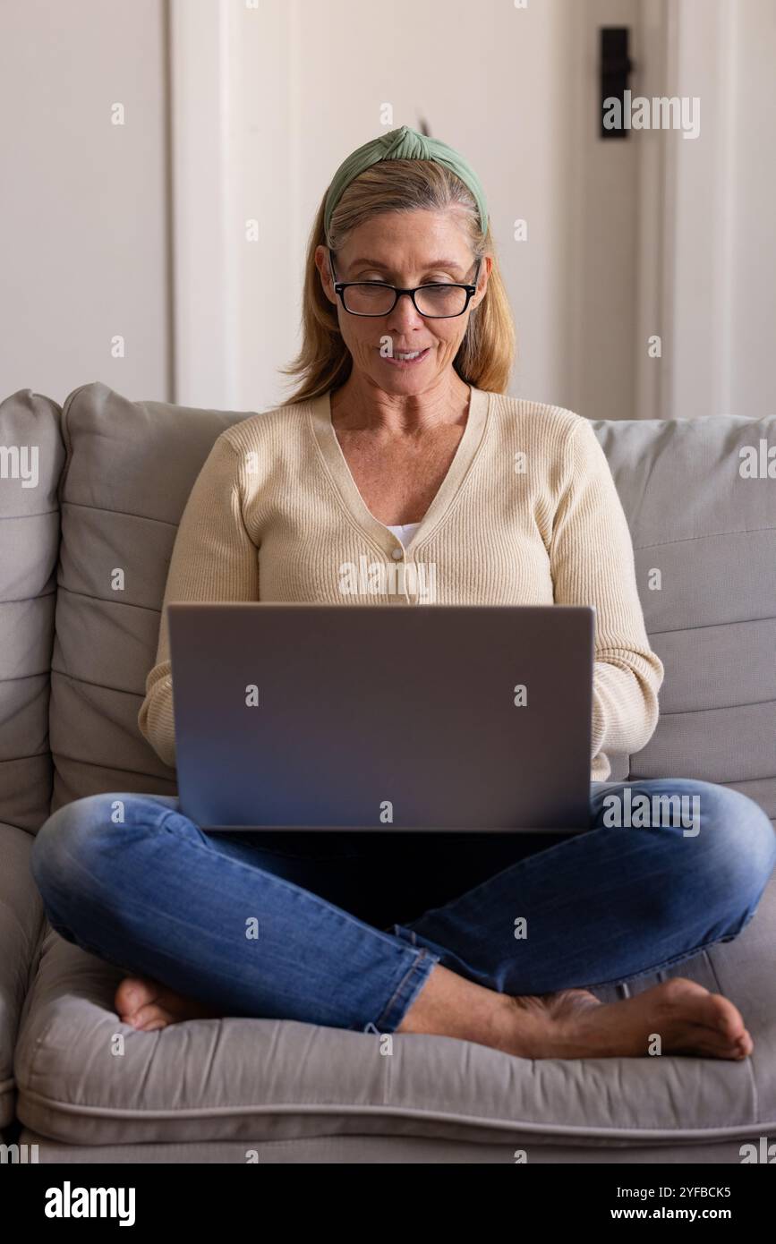 senior woman using laptop at home, sitting comfortably on sofa, smiling Stock Photo