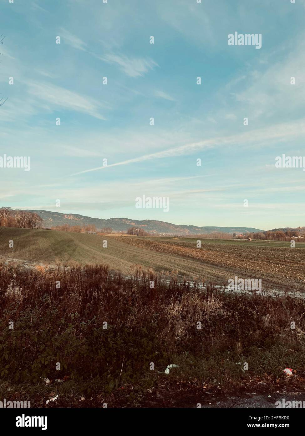 Vast, open fields stretch toward distant hills under a soft, pastel sky—capturing the quiet beauty of rural landscapes at dusk. - Smartphone Captured Stock Image