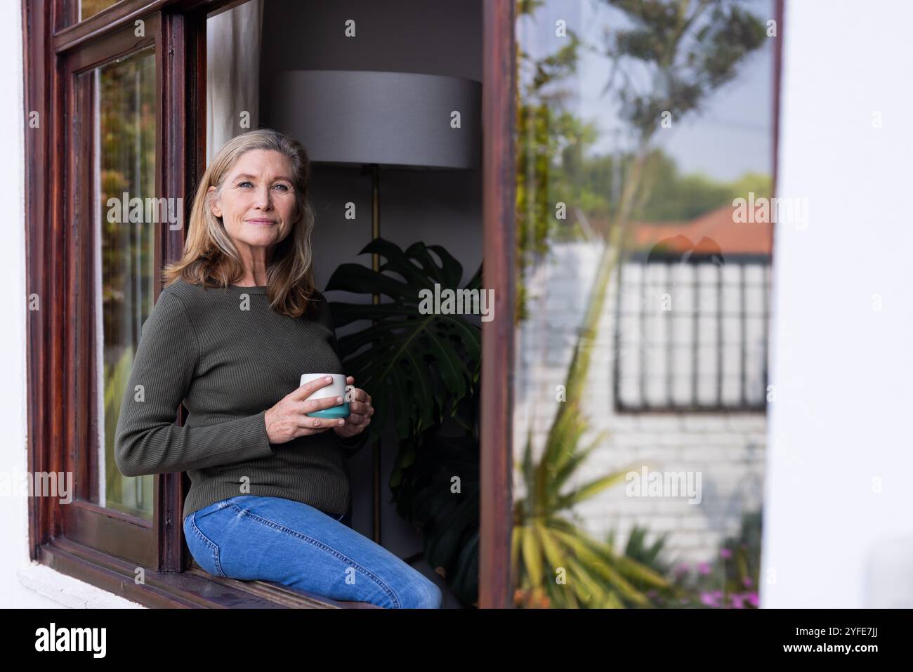 Relaxing at home, senior woman drinking coffee while looking out window Stock Photo
