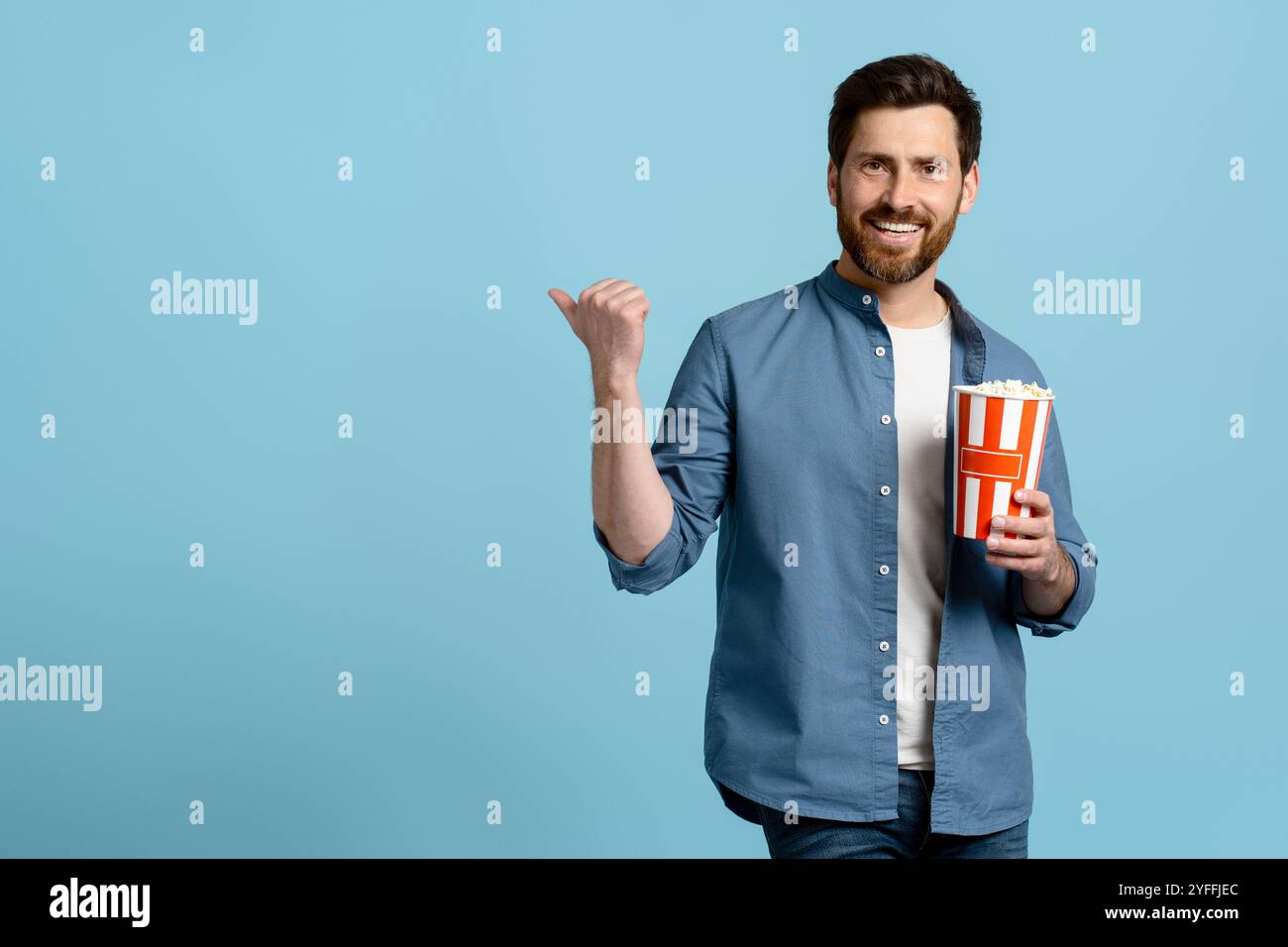 Man holding a popcorn bucket is pointing his finger to the empty space ...