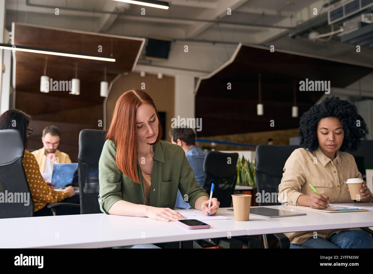 Young office workers are concentrating on their work while sitting at desks in a modern co working space Stock Photo