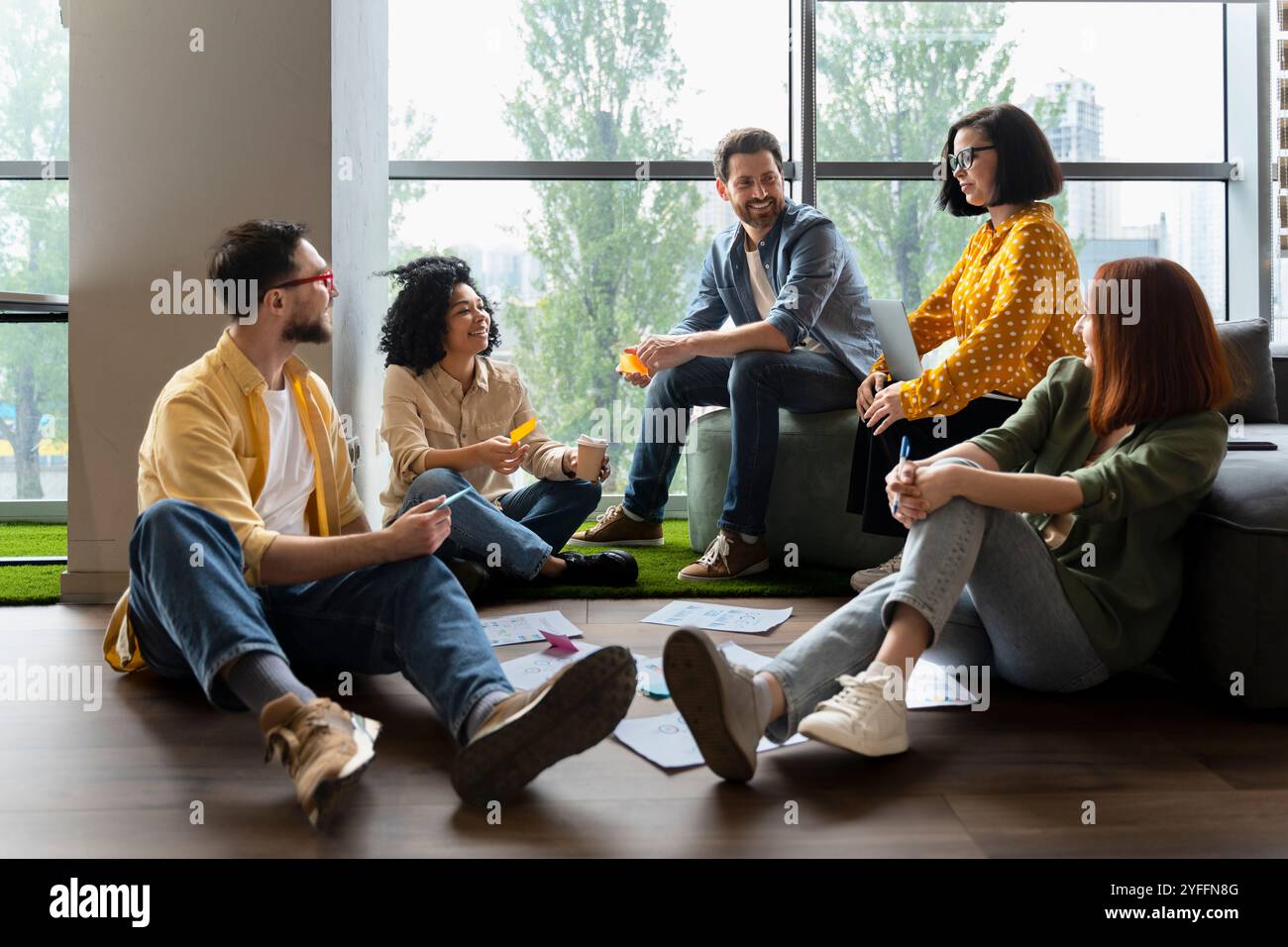 Diverse team of professionals is having a productive brainstorming session, sitting on the floor and discussing new ideas Stock Photo