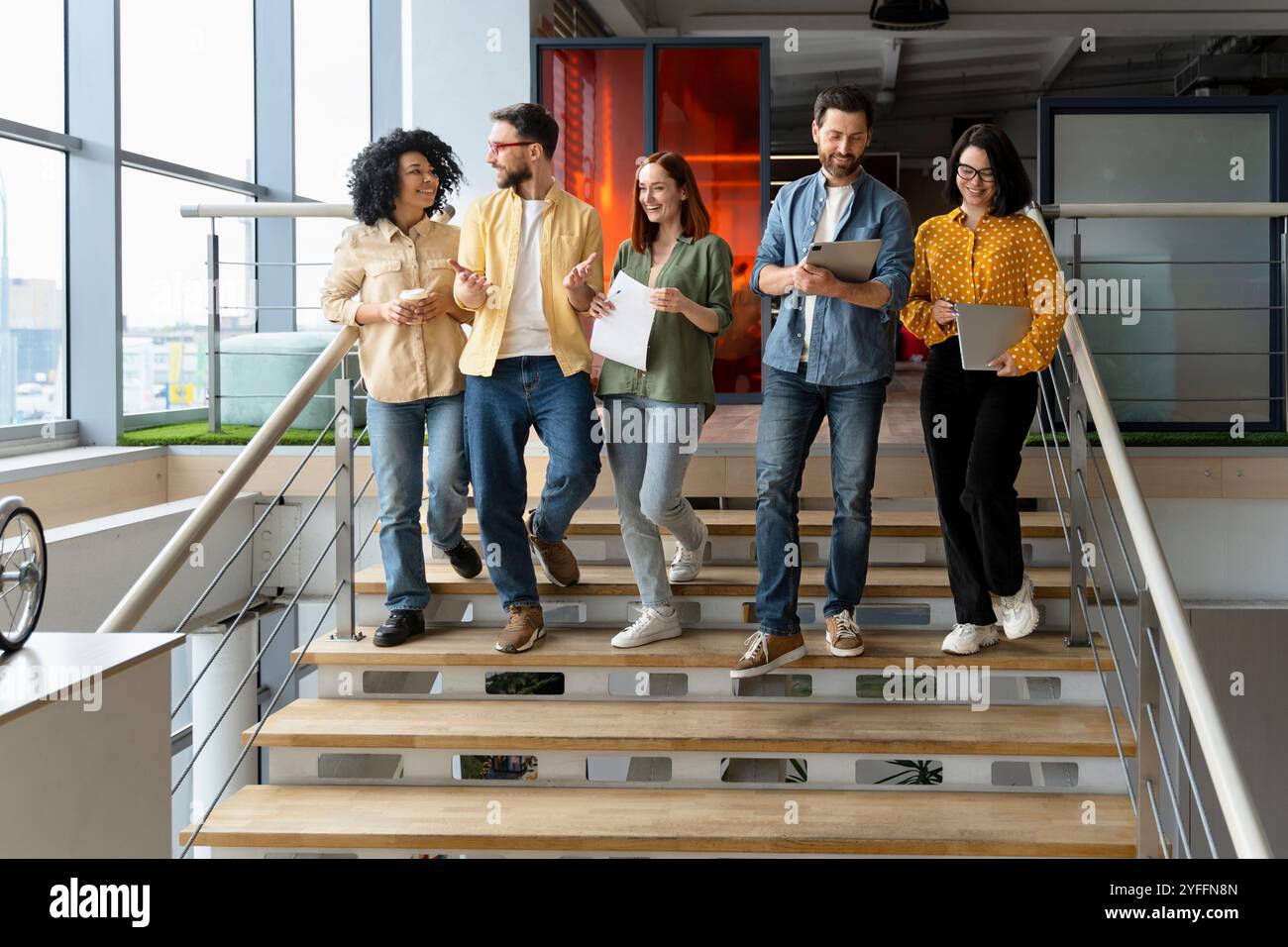 Diverse group of business people are having a discussion while walking down a staircase in a modern office Stock Photo