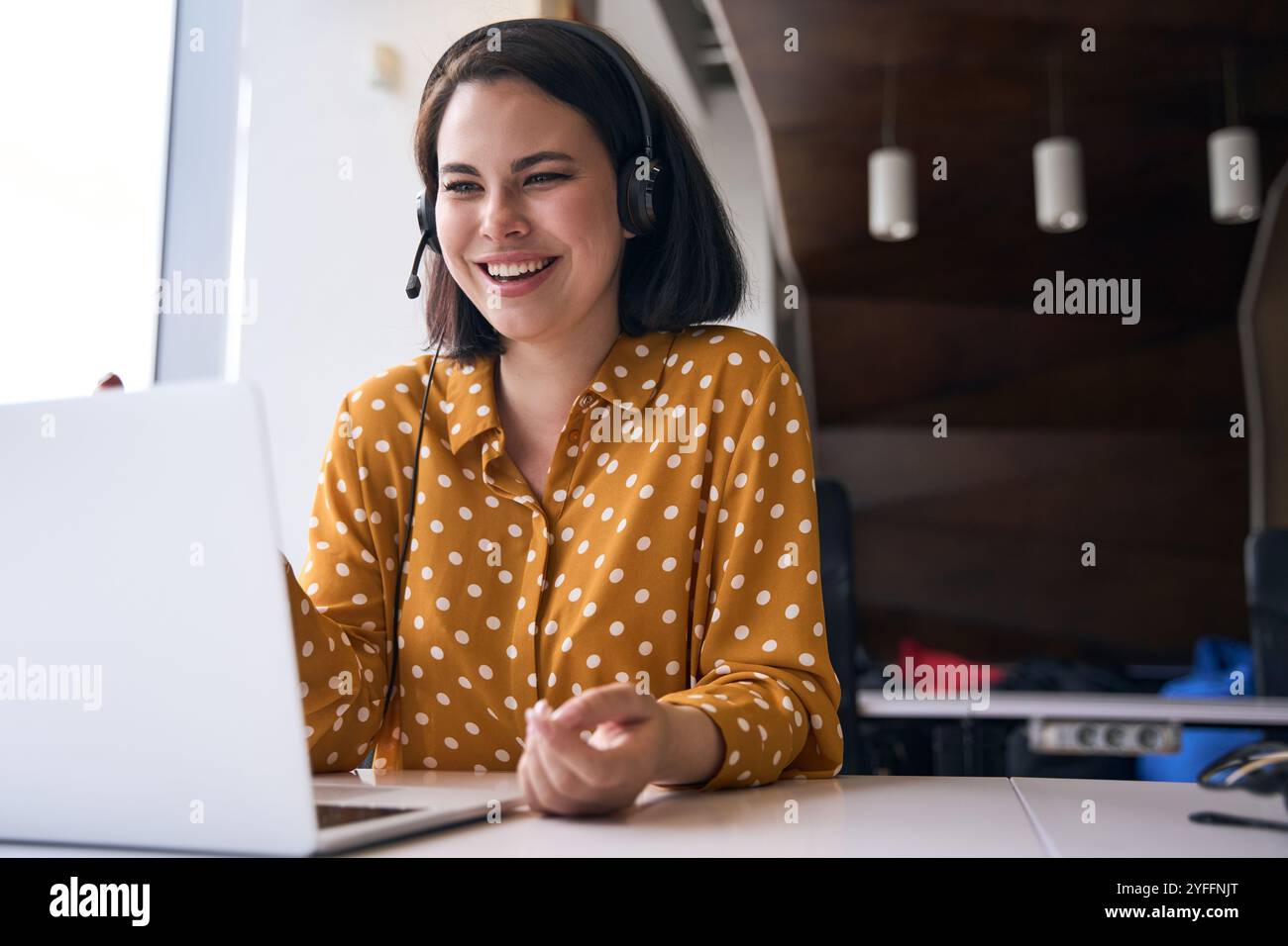 Cheerful businesswoman wearing headset is having a video call on laptop in the office Stock Photo
