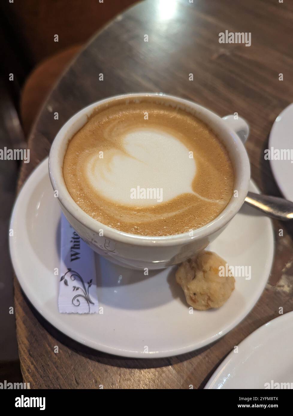 Cup of cappuccino at a local coffee shop with a cookie on the side. - Smartphone Captured Stock Image
