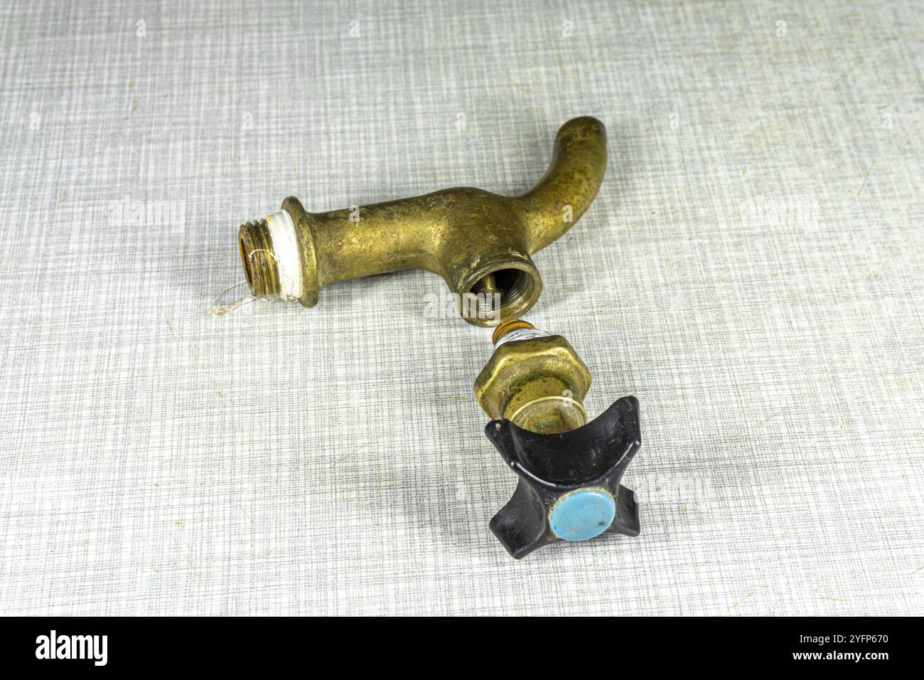 An old bronze disassembled water tap with a plastic valve with the remains of a silicone sealant on the thread lies on a light surface Stock Photo