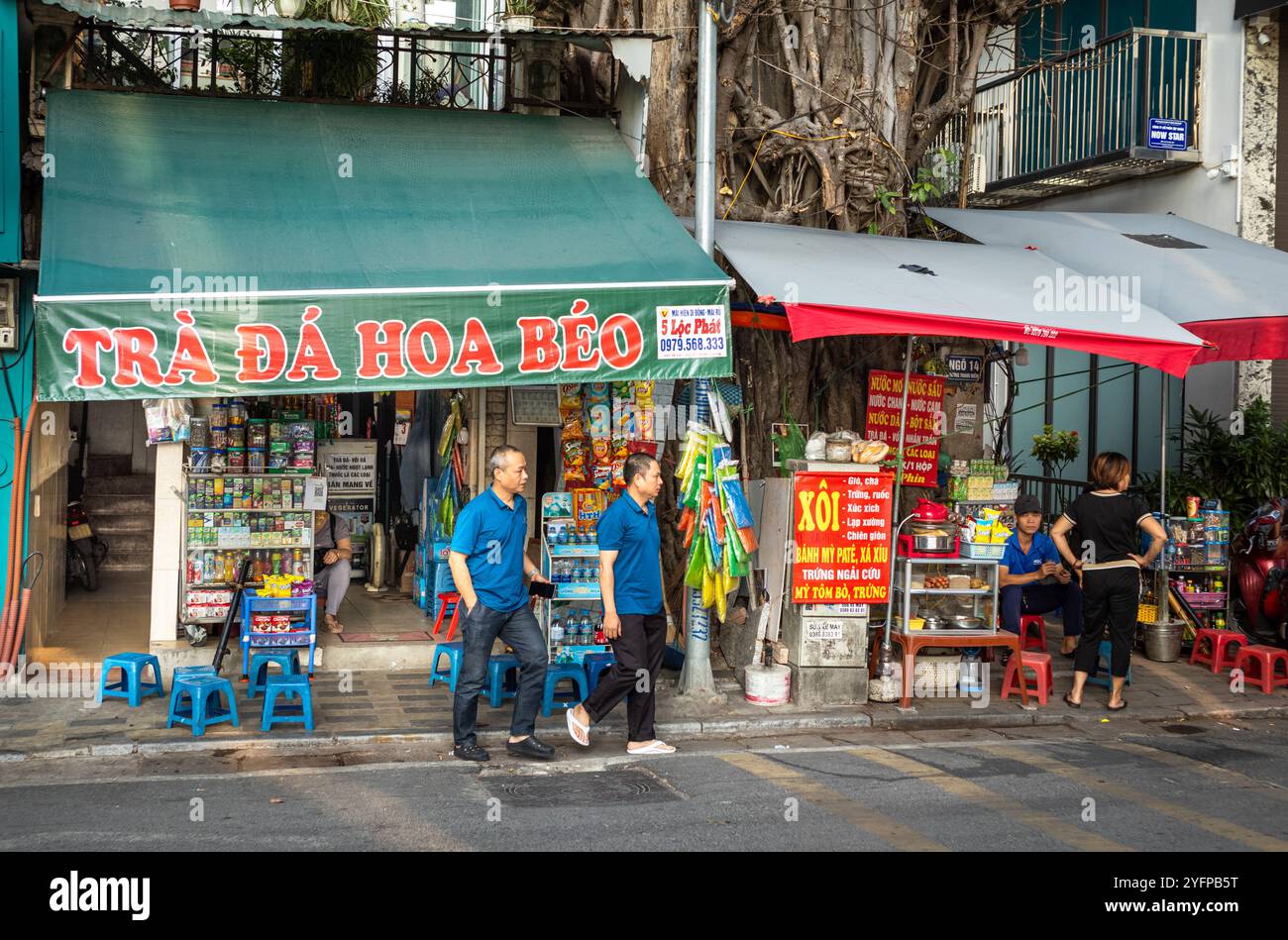 Two men walk out of a small shop selling iced tea and groceries on Yen Phu Street in Hanoi, Vietnam Stock Photo