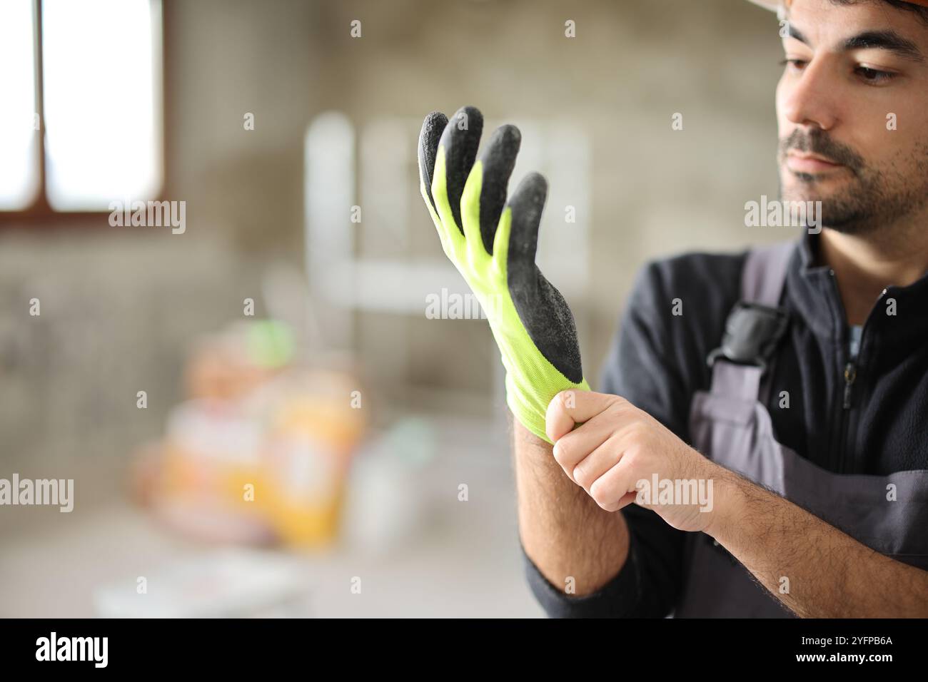 Construction worker putting on protective gloves in a house under renovation Stock Photo