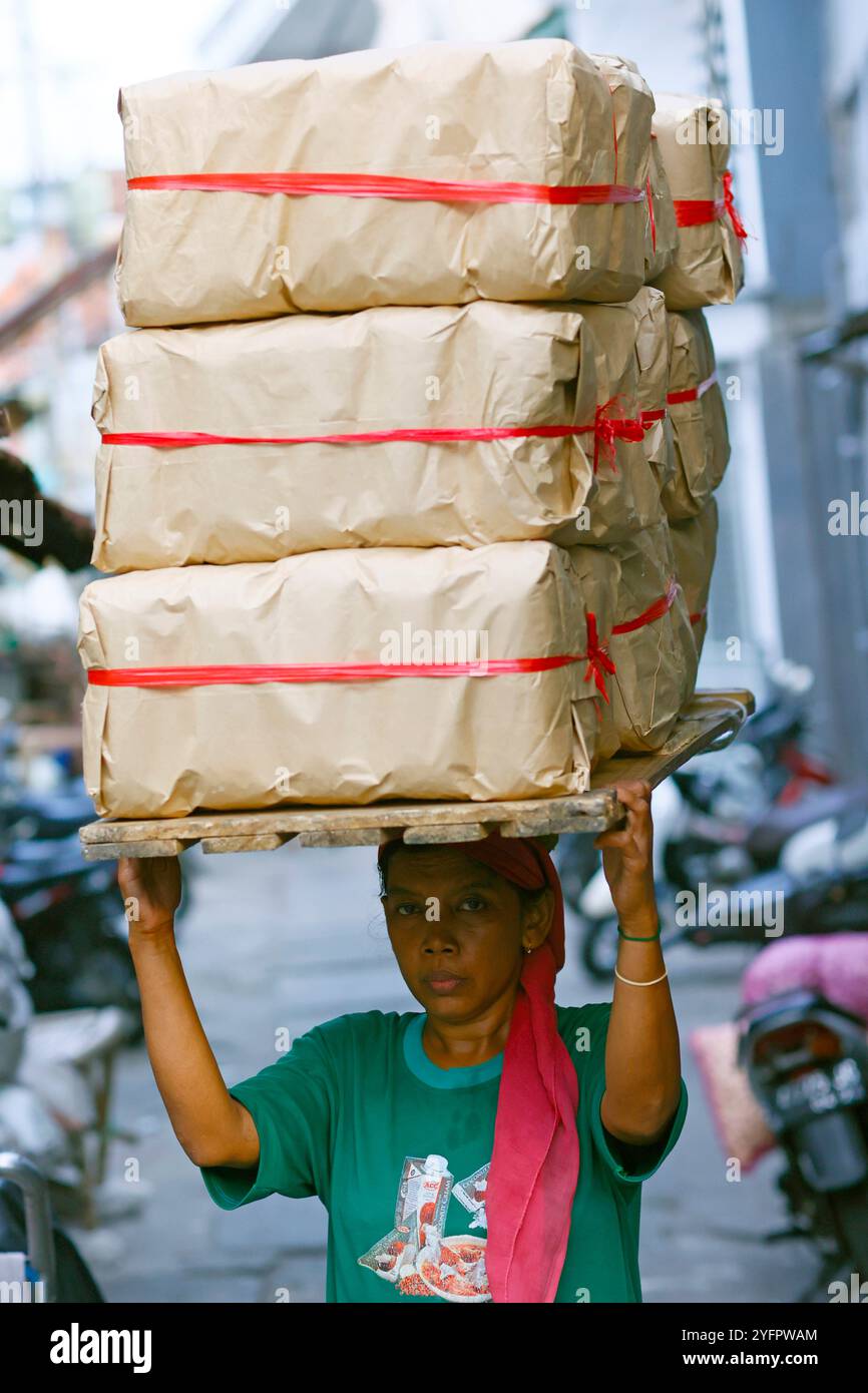 Daily worker at traditional food market.  Woman carrying heavy bags with  on her head.  Surabaya. Indonesia. Stock Photo