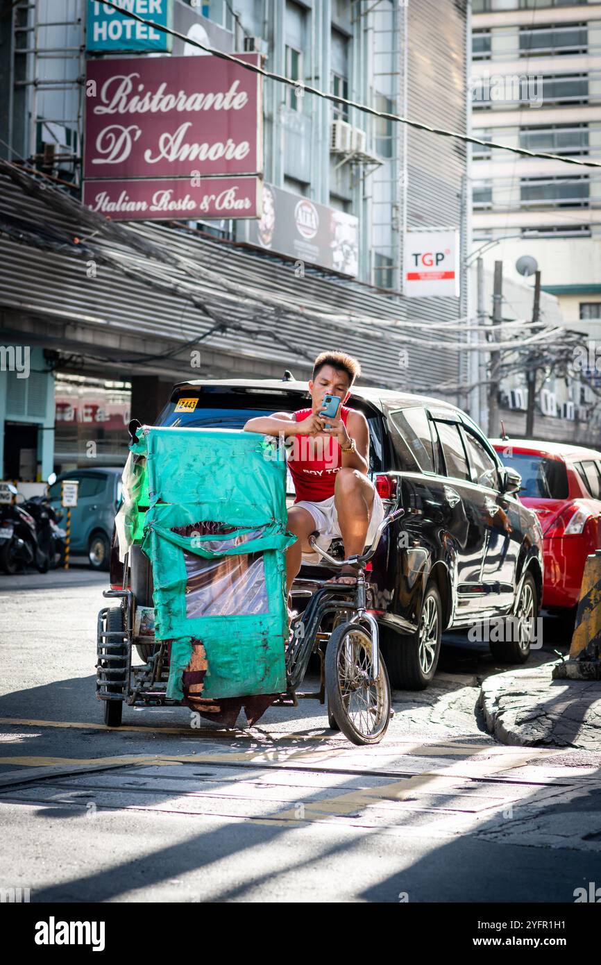 A young filipino man takes a break sat on his trike and checks his phone in Manila,The Philippines. Stock Photo