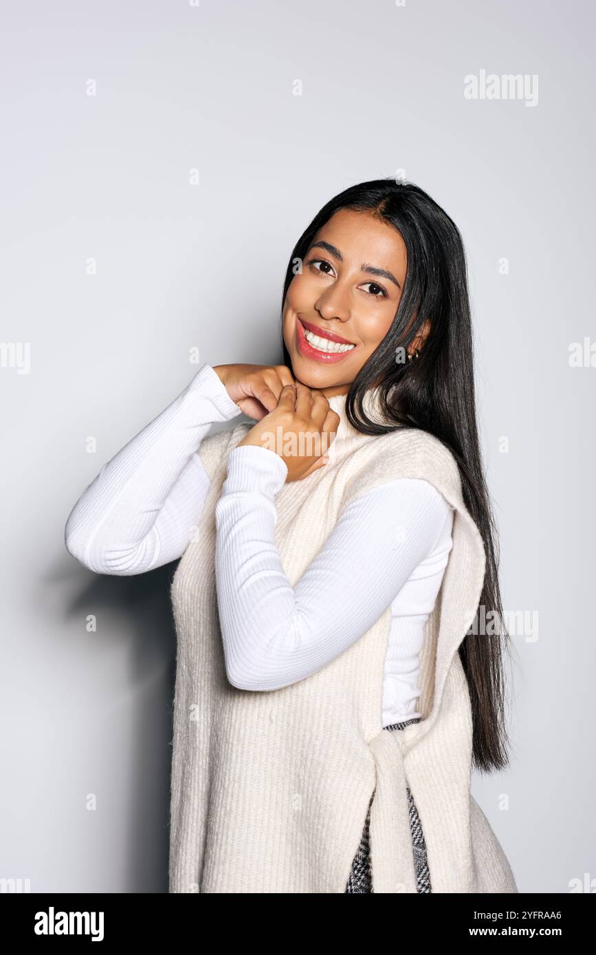 The cheerful young woman smiles warmly while adjusting her outfit in a ...