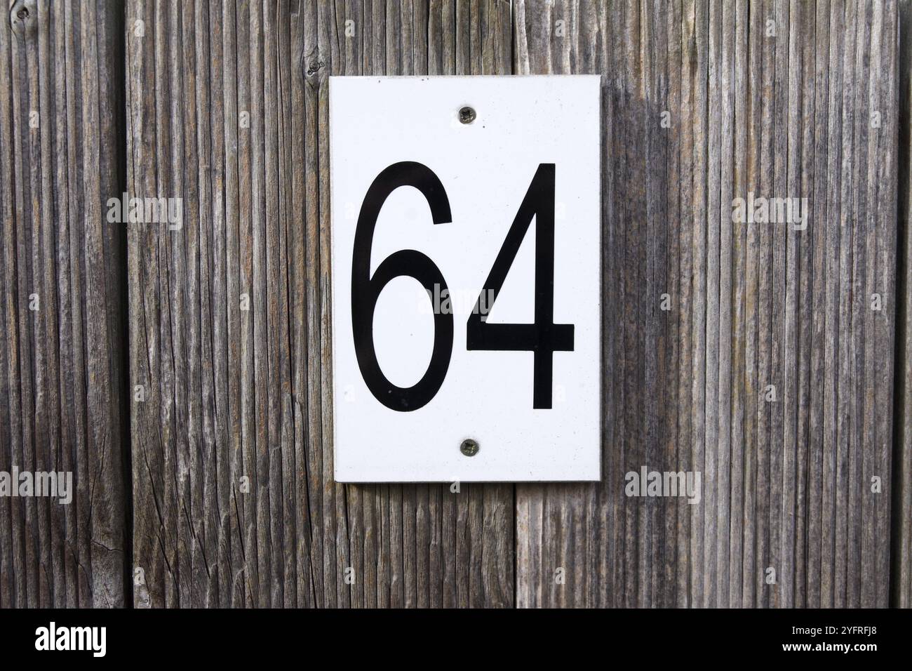 64, number, sixty-four, sign, The numbers 6 and 4 are written in black numbers on a white sign. The sign is attached to a wooden fence Stock Photo