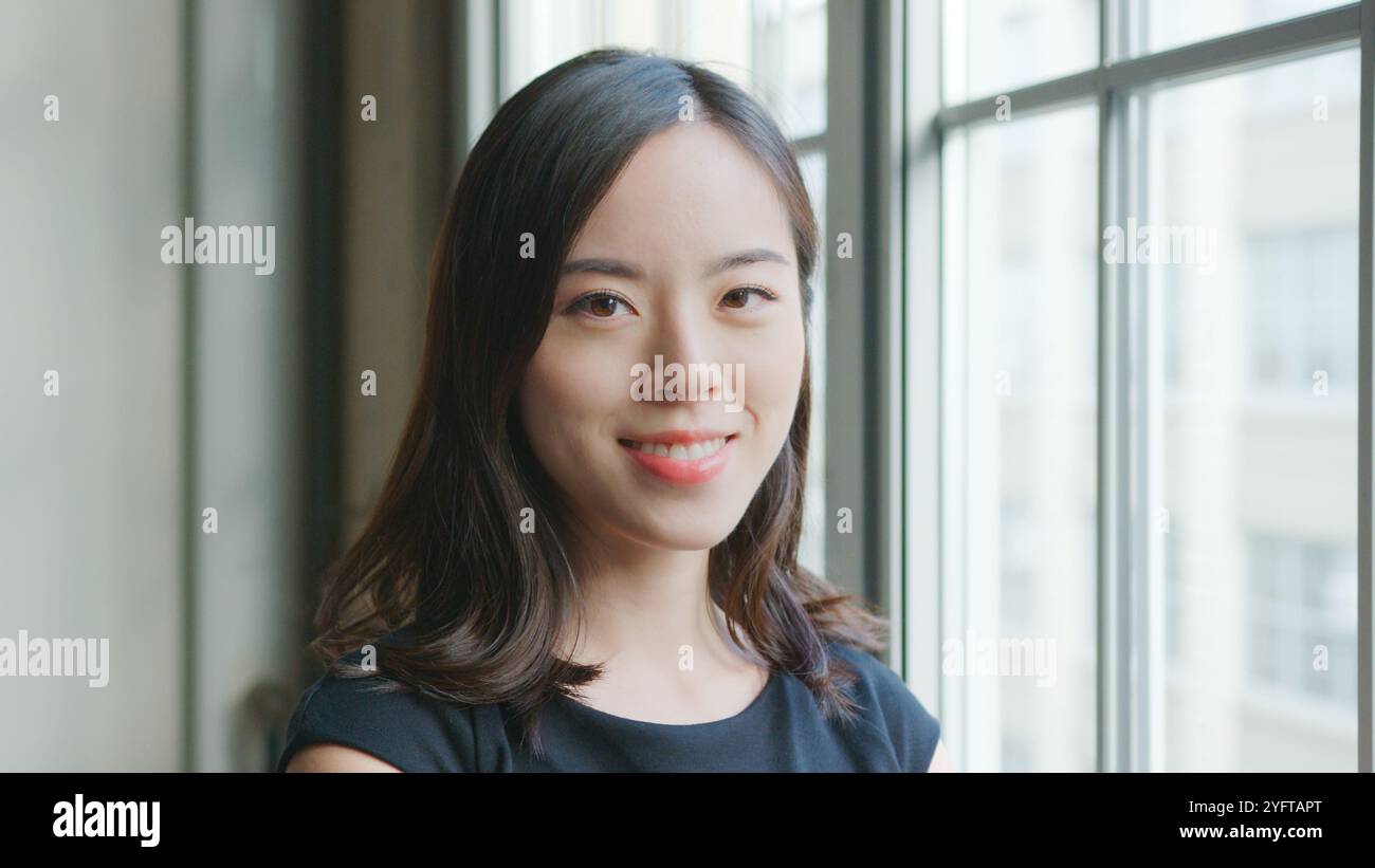 Head And Shoulders Portrait Of Smiling Young Businesswoman Standing By Window In Office Stock Photo
