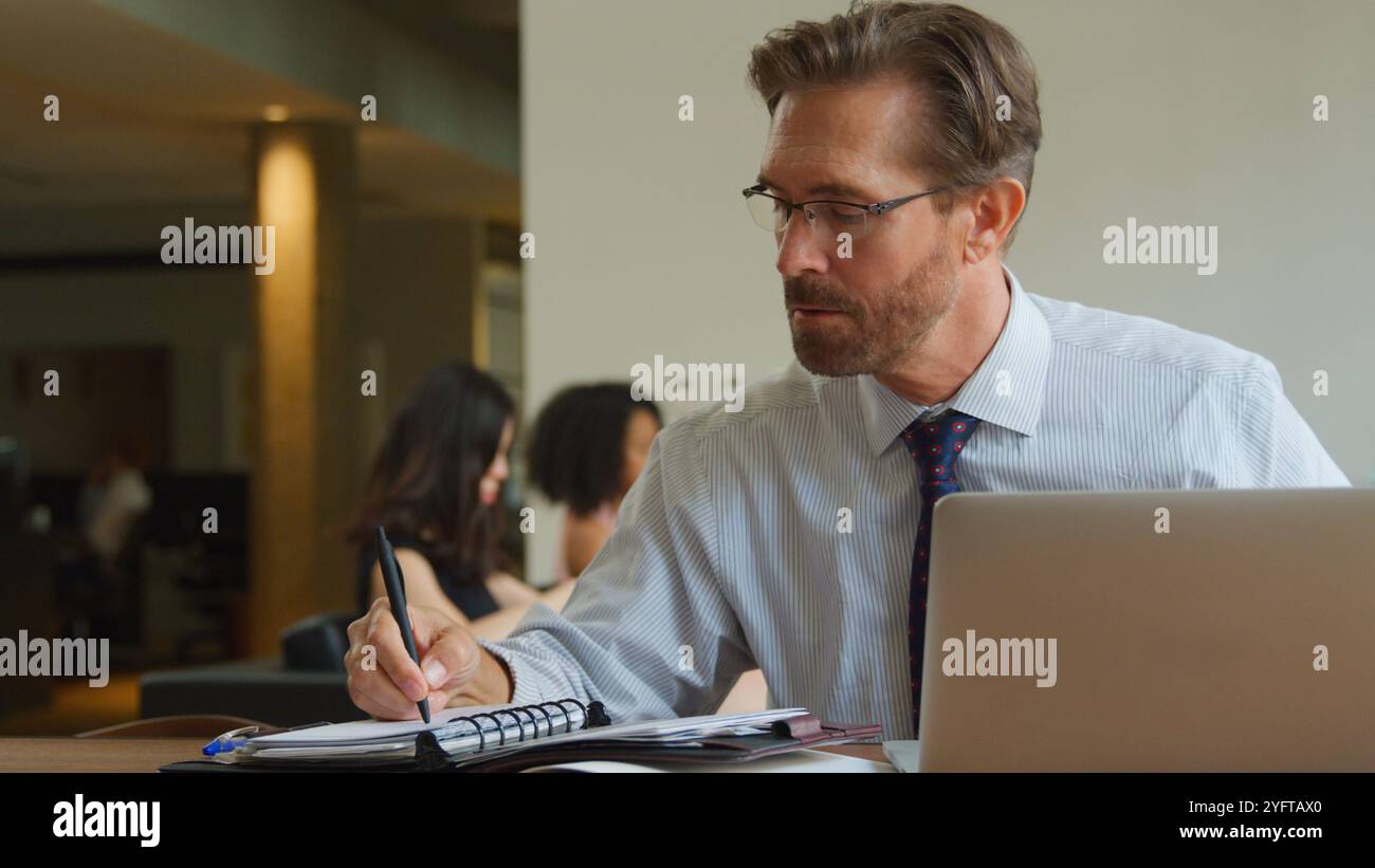 Mature Businessman In Informal Seating Area Of Modern Office Working On Laptop Stock Photo
