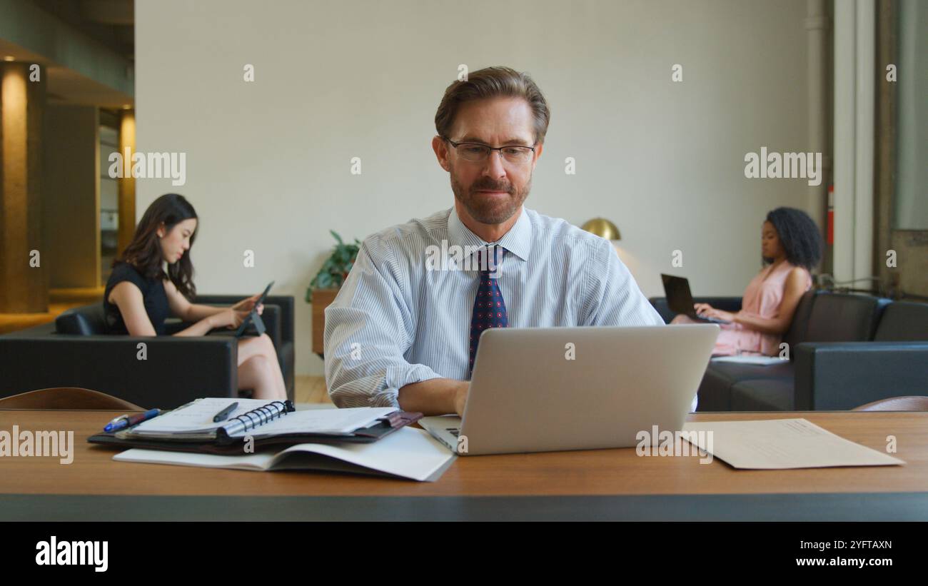 Mature Businessman In Informal Seating Area Of Modern Office Working On Laptop Stock Photo