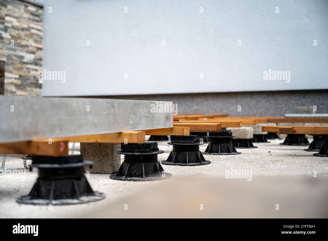 A close-up of an elevated deck under construction, showing wooden beams supported by adjustable plastic pedestals on a concrete surface, creating a st Stock Photo