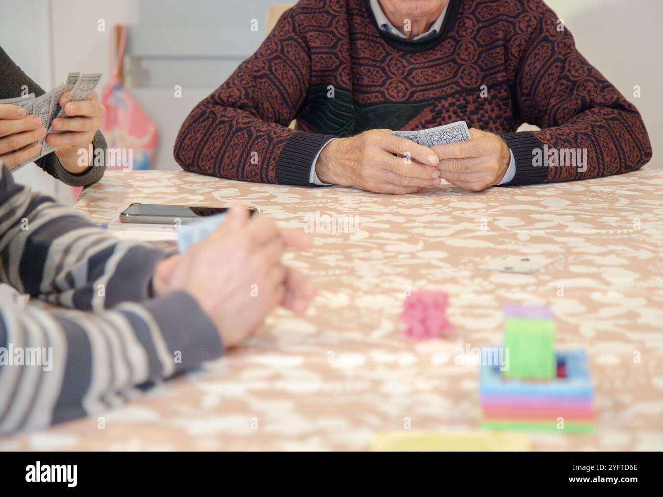 A group of people gather around a table playing cards, a casual game with family or friends, promoting social interaction Stock Photo