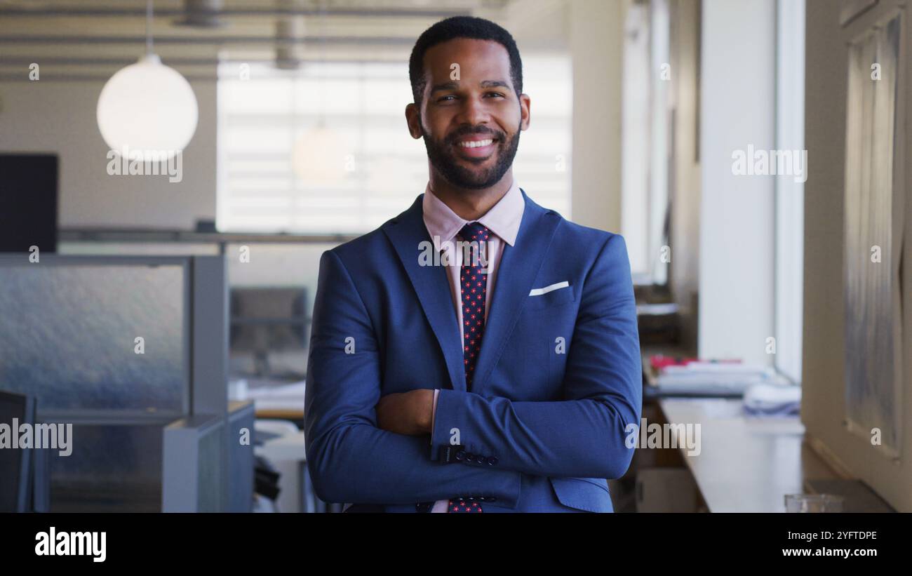 Portrait Of Smiling Businessman With Folded Arms Wearing Suit Working In Empty Open Plan Office Stock Photo