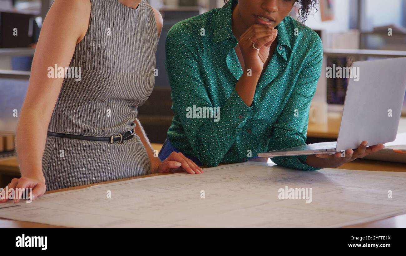 Close Up Of Two Female Architects Meeting In Office With Laptop Studying Building Plans Or Drawings Stock Photo