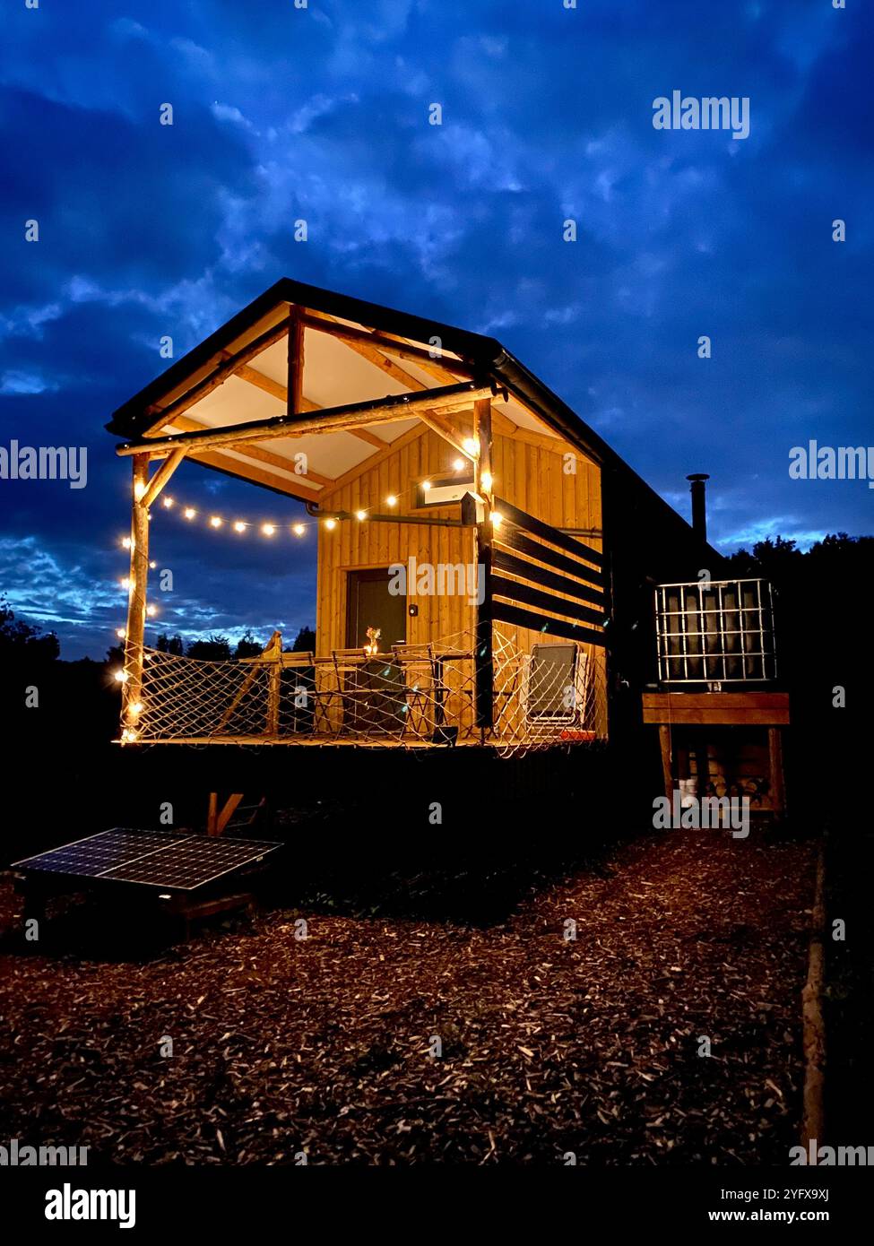 Cozy Wooden Tiny House, Cabin Illuminated with String Lights at Night - Smartphone Captured Stock Image