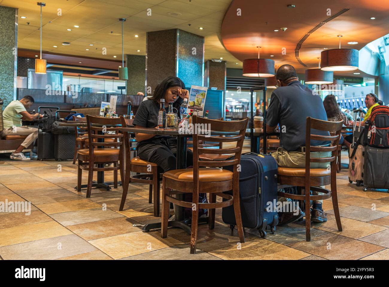 Travelers sitting with luggage in an airport restaurant, awaiting flights and enjoying meals. Miami. USA. Stock Photo