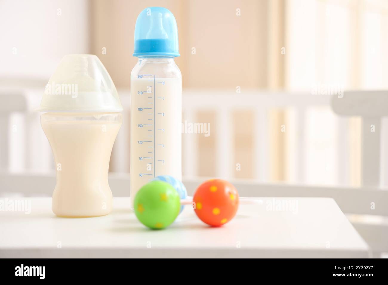 Bottles of baby milk formula and rattle on light table in children's ...