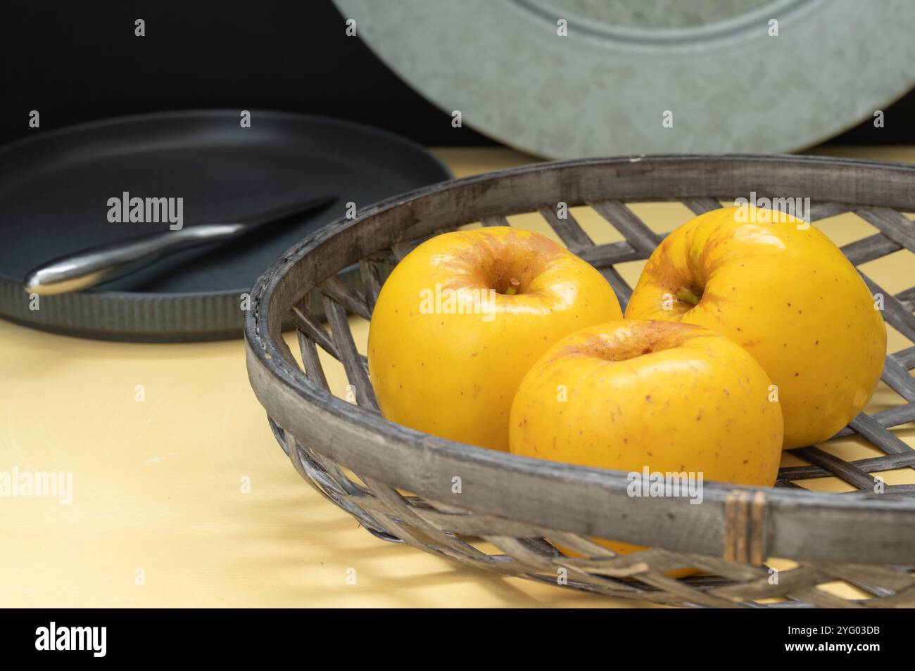 Three opal apples sit in a basket on a yellow table. Stock Photo